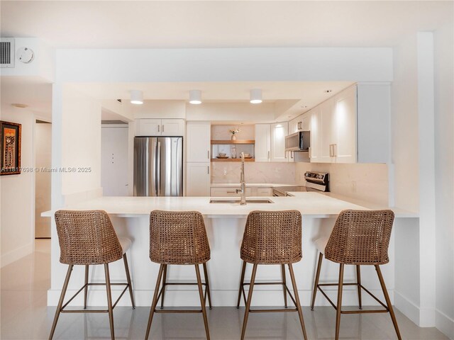 5701 Collins Ave Unit 307, Miami Beach, FL 33140 - kitchen with appliances with stainless steel finishes, a peninsula, light countertops, backsplash, and a kitchen bar