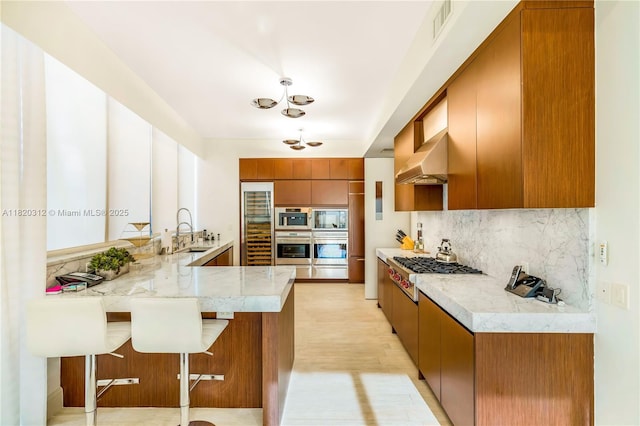 9705 Collins Ave Unit 1101N, Bal Harbour, FL 33154 - kitchen with a peninsula, brown cabinets, range hood, appliances with stainless steel finishes, and backsplash