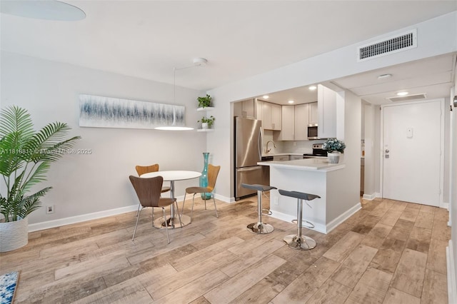 2781 Taft St Unit 308, Hollywood, FL 33020 - kitchen featuring appliances with stainless steel finishes, light countertops, light wood-style flooring, a kitchen breakfast bar, and a peninsula