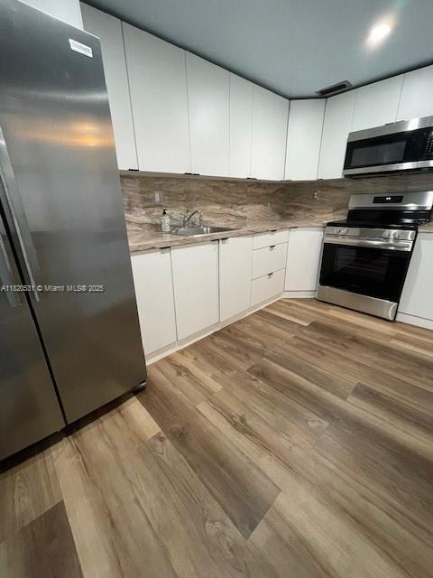 1475 NE 125th Ter Unit 614K, North Miami, FL 33161 - kitchen with appliances with stainless steel finishes, white cabinetry, light wood-style floors, decorative backsplash, and light countertops