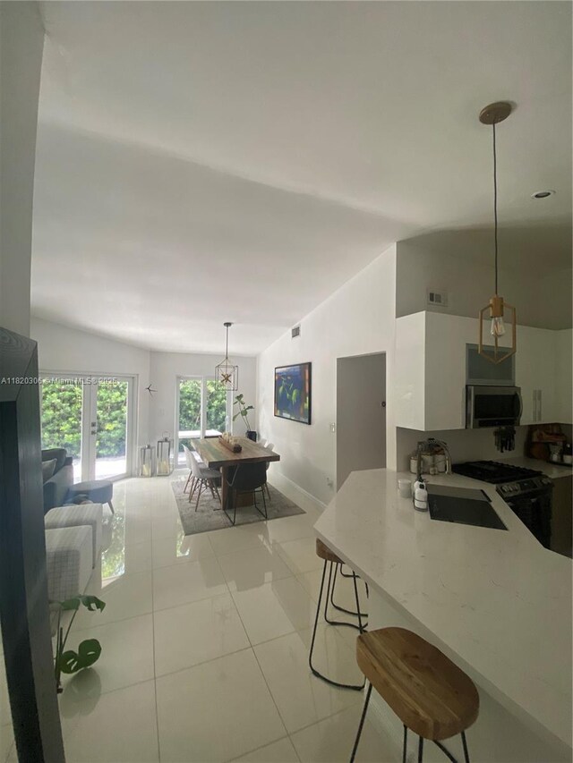 10090 NW 57th St, Doral, FL 33178 - kitchen with stainless steel microwave, white cabinetry, light countertops, hanging light fixtures, and a breakfast bar area