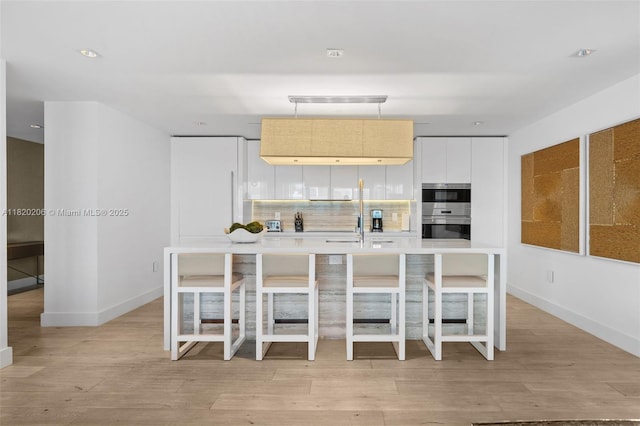 102 24th St Unit Ph-1706, Miami Beach, FL 33139 - kitchen with a kitchen island with sink, modern cabinets, light countertops, light wood-style flooring, and decorative light fixtures