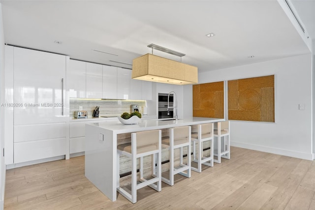 102 24th St Unit Ph-1706, Miami Beach, FL 33139 - kitchen with light countertops, light wood-style floors, an island with sink, decorative backsplash, and modern cabinets