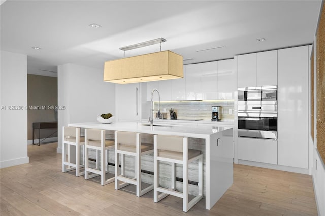 102 24th St Unit Ph-1706, Miami Beach, FL 33139 - kitchen featuring light wood-type flooring, modern cabinets, a kitchen island with sink, light countertops, and a kitchen breakfast bar