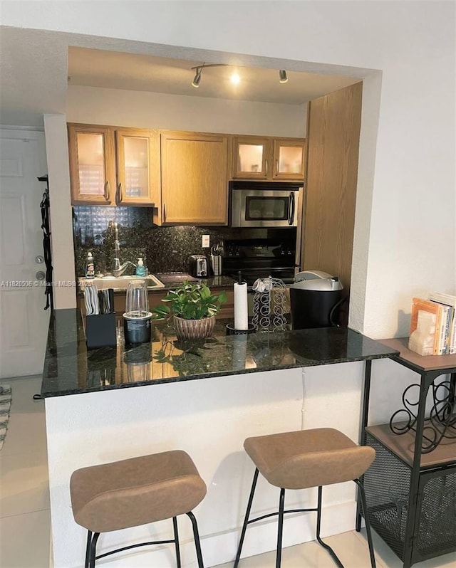 445 SW 11th St Unit 101, Miami, FL 33130 - kitchen with range, stainless steel microwave, decorative backsplash, a kitchen breakfast bar, and glass insert cabinets