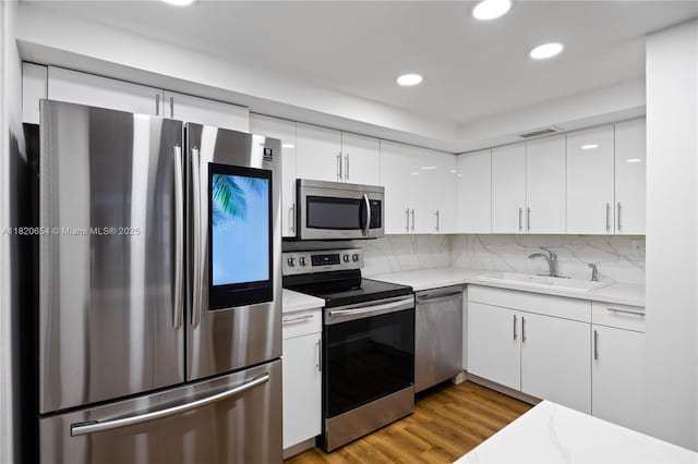 1440 Brickell Bay Unit 307, Miami, FL 33131 - kitchen with stainless steel appliances, white cabinets, recessed lighting, wood finished floors, and backsplash