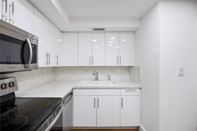 1440 Brickell Bay Unit 307, Miami, FL 33131 - kitchen with appliances with stainless steel finishes, white cabinets, backsplash, modern cabinets, and light stone counters