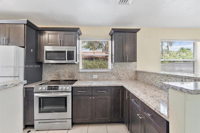 602 El Prado, West Palm Beach, FL 33405 - kitchen featuring stainless steel appliances, tasteful backsplash, light stone counters, light tile patterned floors, and dark brown cabinets