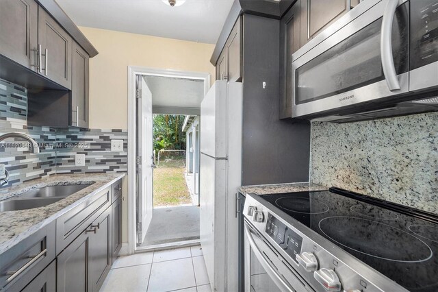 602 El Prado, West Palm Beach, FL 33405 - kitchen with stainless steel appliances, light stone counters, light tile patterned floors, decorative backsplash, and dark brown cabinets