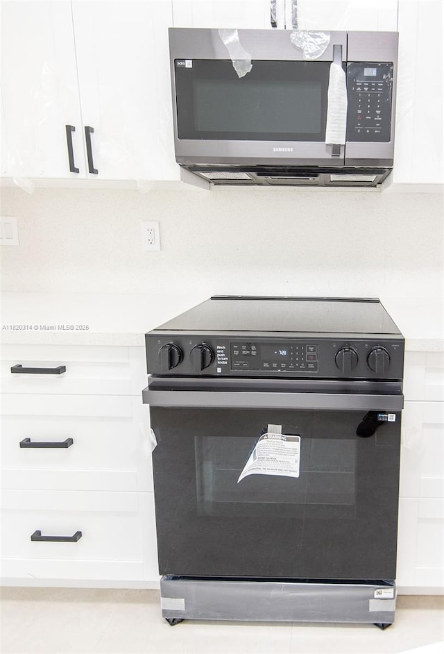 1750 NE 191st St Unit 100-1, Miami, FL 33179 - kitchen view of black electric range oven, stainless steel microwave, white cabinets, and light countertops
