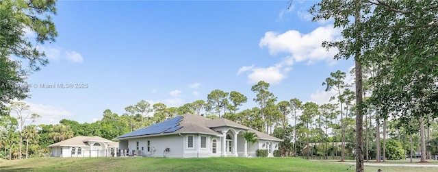 17038 N 61st Pl N, Loxahatchee, FL 33470 - view of side of property with roof mounted solar panels, a lawn, stucco siding, and view of wooded area
