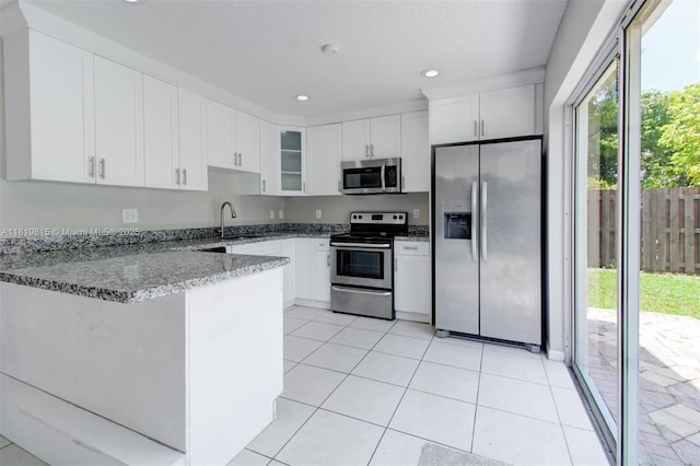 9741 SW 12th St, Pembroke Pines, FL 33025 - kitchen featuring stainless steel appliances, a peninsula, light stone countertops, light tile patterned floors, and glass insert cabinets