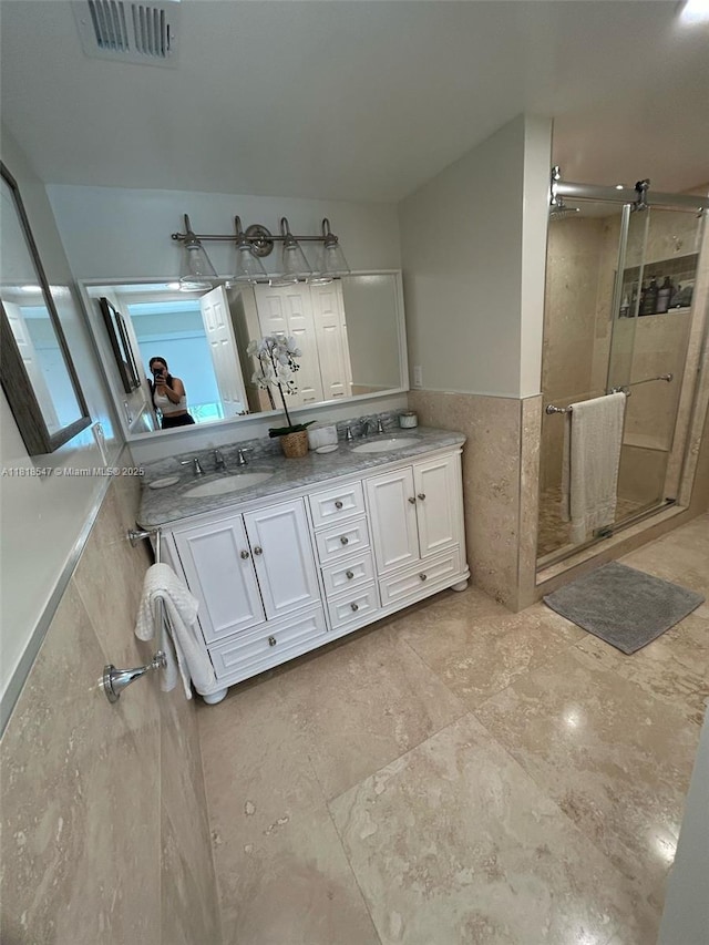 4000 NE 168th St Unit 110A, North Miami Beach, FL 33160 - bathroom featuring a stall shower, double vanity, tile walls, and a wainscoted wall
