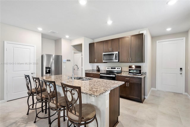 5720 Mentmore Dr, Mangonia Park, FL 33407 - kitchen featuring appliances with stainless steel finishes, dark brown cabinets, a kitchen breakfast bar, a center island with sink, and light stone counters