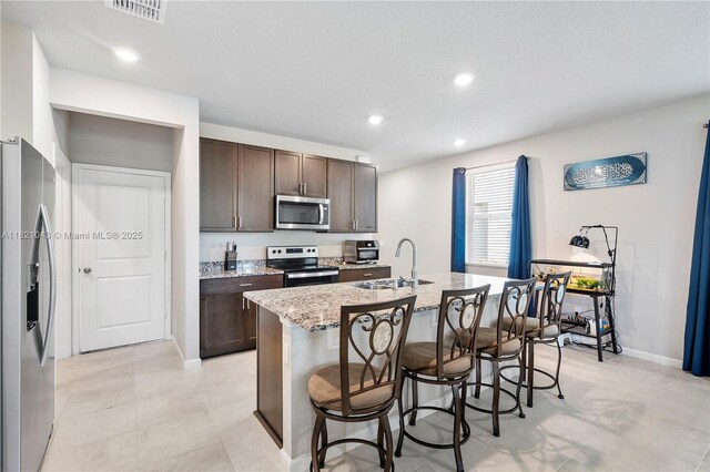 5720 Mentmore Dr, Mangonia Park, FL 33407 - kitchen with stainless steel appliances, an island with sink, dark brown cabinets, a breakfast bar, and recessed lighting