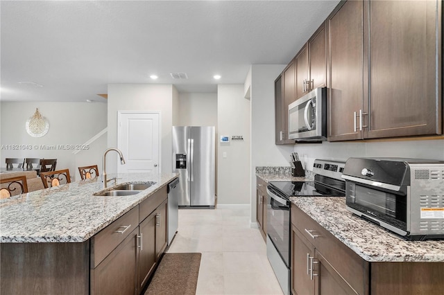 5720 Mentmore Dr, Mangonia Park, FL 33407 - kitchen with stainless steel appliances, dark brown cabinetry, light stone countertops, an island with sink, and light tile patterned flooring