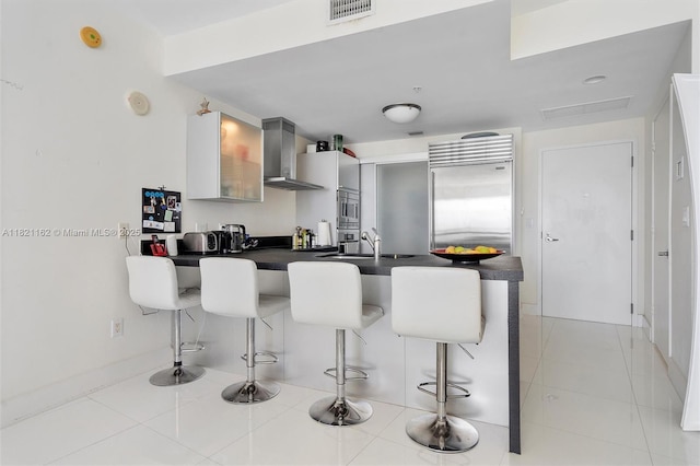 18201 Collins Ave Unit 2008, Sunny Isles Beach, FL 33160 - kitchen featuring wall chimney exhaust hood, appliances with stainless steel finishes, a peninsula, dark countertops, and a breakfast bar