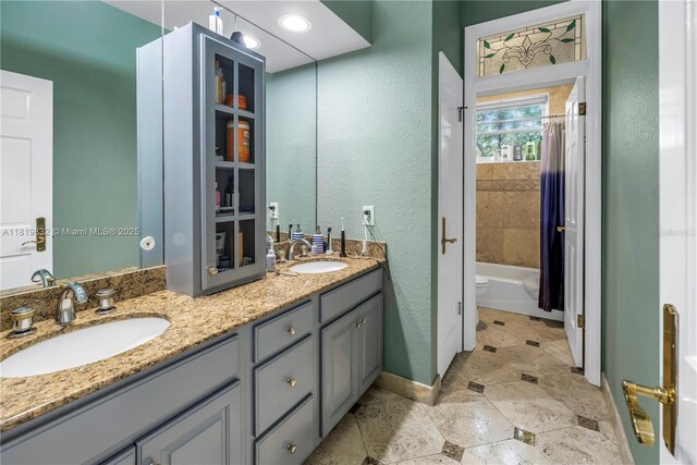 8755 Commodore Dr, Seminole, FL 33776 - bathroom featuring double vanity, stone finish flooring, shower / bath combo with shower curtain, and a textured wall
