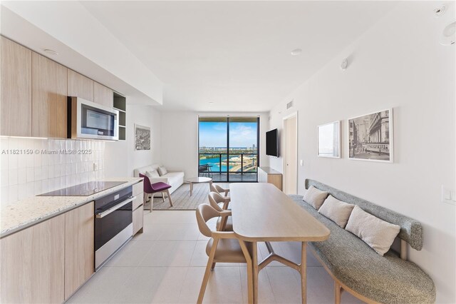 159 NE 6th St Unit 3016, Miami, FL 33132 - kitchen with wall oven, light brown cabinets, black electric stovetop, open floor plan, and a wall of windows