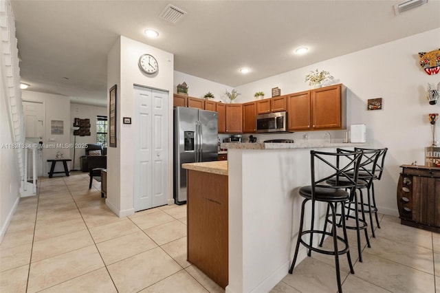 3507 W 89th Pl, Hialeah, FL 33018 - kitchen with stainless steel appliances, a peninsula, brown cabinetry, a kitchen breakfast bar, and light tile patterned floors