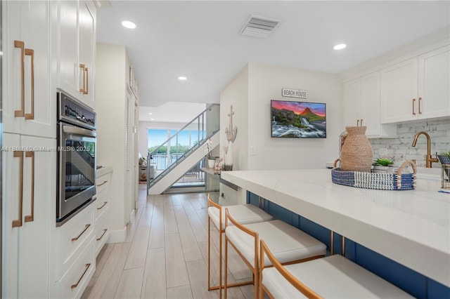 4034 N Ocean Dr, Hollywood, FL 33019 - kitchen with stainless steel oven, a kitchen bar, white cabinetry, tasteful backsplash, and recessed lighting