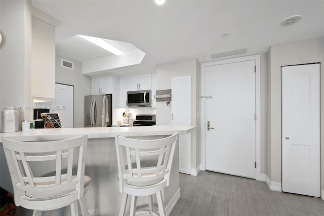 888 Brickell Key Dr Unit 1006, Miami, FL 33131 - kitchen with appliances with stainless steel finishes, light countertops, a peninsula, light wood finished floors, and white cabinetry