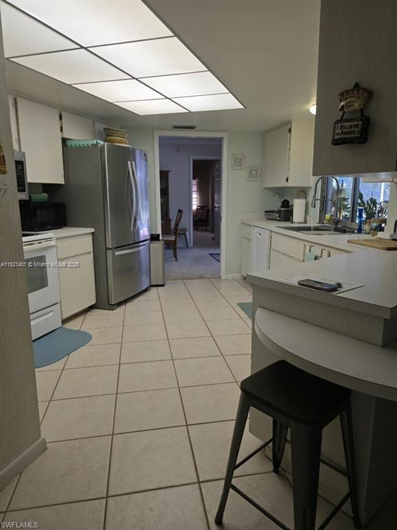 13001 Shetland Ln, Fort Myers, FL 33912 - kitchen with stainless steel appliances, light countertops, light tile patterned flooring, white cabinetry, and a breakfast bar