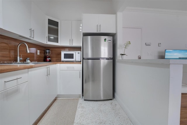 1200 Euclid Ave Unit 103, Miami Beach, FL 33139 - kitchen with freestanding refrigerator, white microwave, tasteful backsplash, white cabinetry, and dark aggregate flooring
