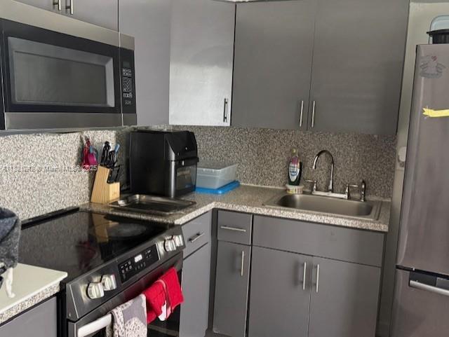 67 NW 34th St, Miami, FL 33127 - kitchen featuring stainless steel appliances, gray cabinetry, decorative backsplash, and light countertops