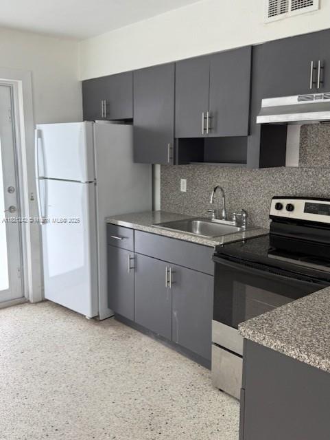 67 NW 34th St, Miami, FL 33127 - kitchen featuring stainless steel electric range oven, under cabinet range hood, tasteful backsplash, freestanding refrigerator, and gray cabinetry