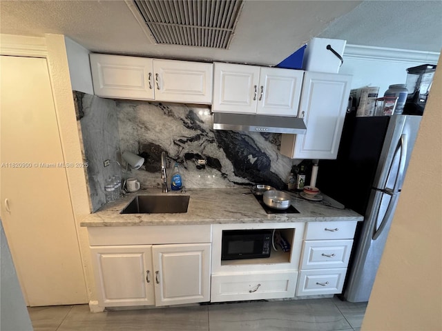 19201 N Collins Ave Unit 826, Sunny Isles Beach, FL 33160 - kitchen with under cabinet range hood, black microwave, backsplash, white cabinetry, and freestanding refrigerator
