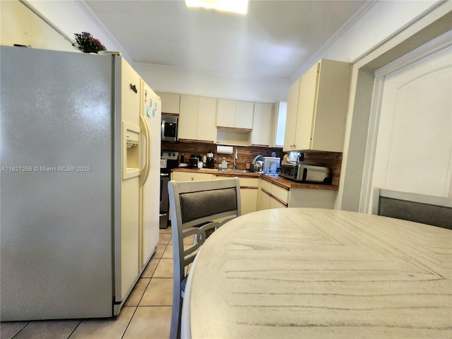 3082 NW 4th St, Miami, FL 33125 - kitchen with stainless steel appliances, light tile patterned flooring, dark countertops, cream cabinetry, and ornamental molding