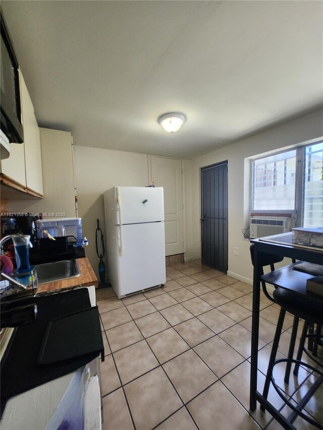 3082 NW 4th St, Miami, FL 33125 - kitchen featuring freestanding refrigerator, light tile patterned floors, white cabinets, and cooling unit