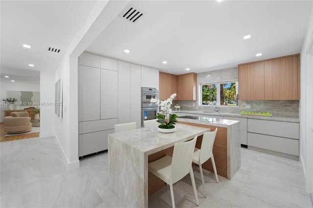 5211 Granada Blvd, Coral Gables, FL 33146 - kitchen with modern cabinets, a kitchen island, double oven, recessed lighting, and backsplash