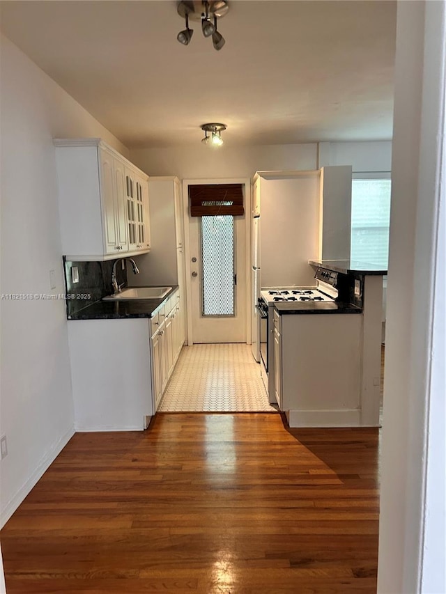 101 Collins Ave Unit 16, Miami Beach, FL 33139 - kitchen with white range with gas stovetop, light wood finished floors, dark countertops, glass insert cabinets, and white cabinets