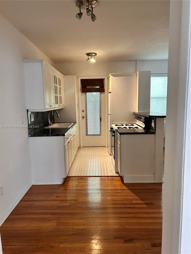 101 Collins Ave Unit 16, Miami Beach, FL 33139 - kitchen with white range with gas stovetop, light wood finished floors, dark countertops, glass insert cabinets, and white cabinets