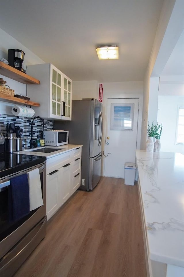 7904 W Dr Unit 501, North Bay Village, FL 33141 - kitchen featuring appliances with stainless steel finishes, wood finished floors, white cabinetry, tasteful backsplash, and glass insert cabinets