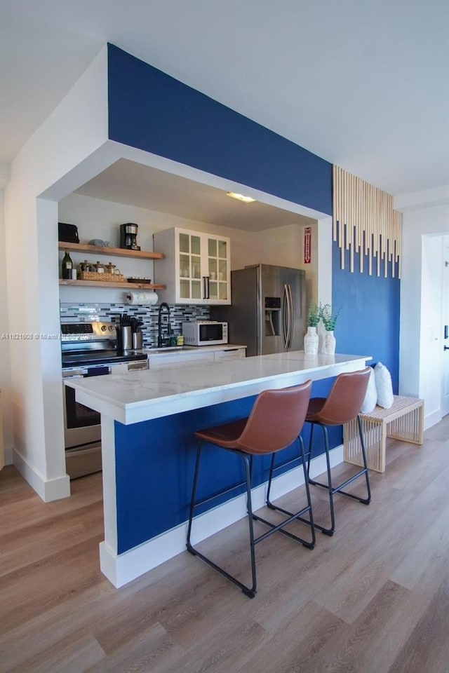7904 W Dr Unit 501, North Bay Village, FL 33141 - kitchen with appliances with stainless steel finishes, light wood-style floors, a kitchen breakfast bar, and backsplash