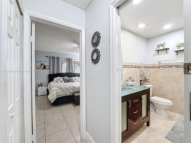1782 W 42nd St Unit 1782, Hialeah, FL 33012 - ensuite bathroom featuring tile patterned floors, a textured ceiling, vanity, tile walls, and a wainscoted wall