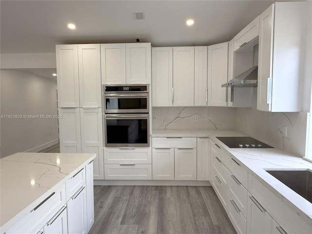 240 SW 55th Ave, Miami, FL 33134 - kitchen with stainless steel double oven, black electric cooktop, white cabinets, wall chimney exhaust hood, and light wood-style flooring