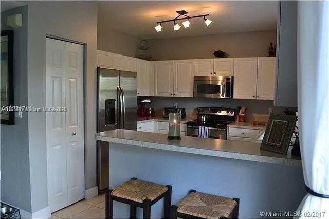 2402 NE 41st Pl, Homestead, FL 33033 - kitchen featuring appliances with stainless steel finishes, a peninsula, white cabinetry, and light tile patterned floors