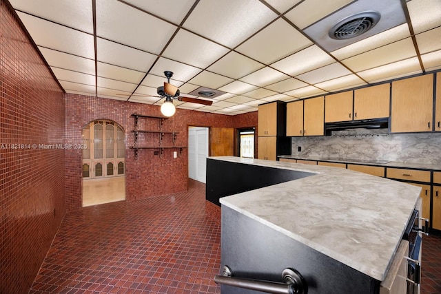 5025 SW 90th Ct, Miami, FL 33165 - kitchen featuring under cabinet range hood, black electric cooktop, a kitchen island, a ceiling fan, and brick wall