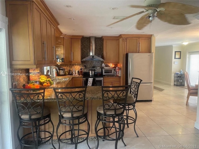 411 Martin Rd, Margate, FL 33068 - kitchen featuring wall chimney exhaust hood, stainless steel appliances, brown cabinets, a peninsula, and ceiling fan