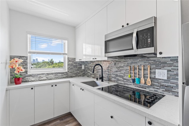 2401 SW 10th St Unit 401, Miami, FL 33135 - kitchen featuring stainless steel microwave, black electric stovetop, backsplash, white cabinets, and wood finished floors
