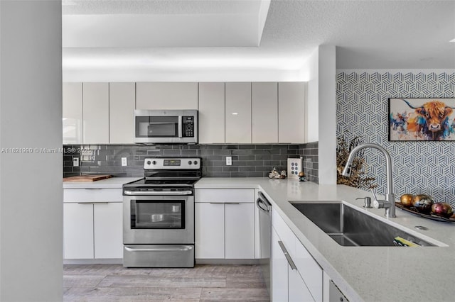 8940 NE 8th Ave Unit 1203, Miami, FL 33138 - kitchen with stainless steel appliances, light wood-style flooring, decorative backsplash, a textured ceiling, and white cabinets