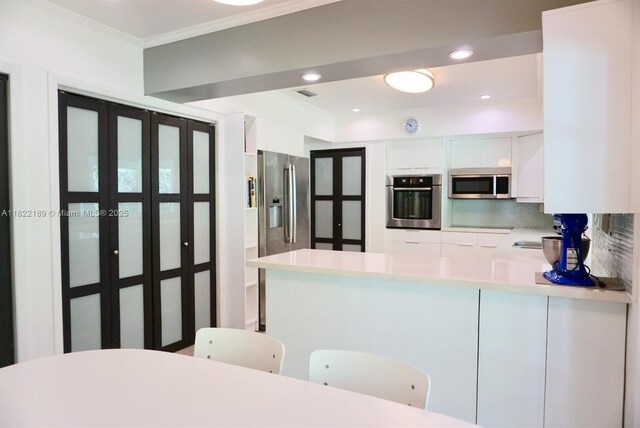 13200 SW 59th Ave, Pinecrest, FL 33156 - kitchen with appliances with stainless steel finishes, white cabinets, tasteful backsplash, a peninsula, and light countertops