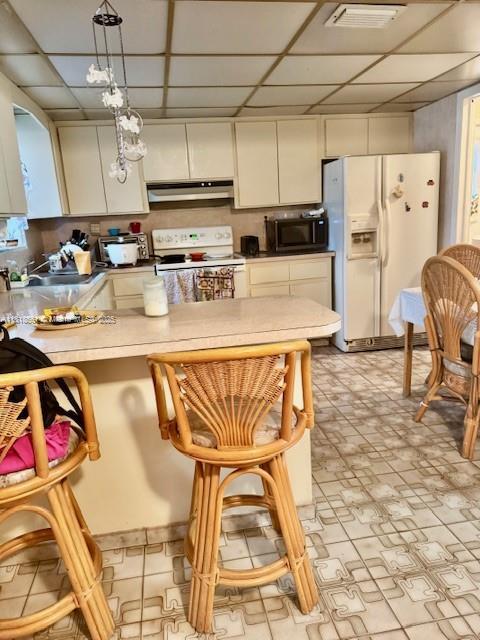 2671 SW 107th Ave, Miami, FL 33165 - kitchen featuring white appliances, under cabinet range hood, a drop ceiling, white cabinets, and hanging light fixtures