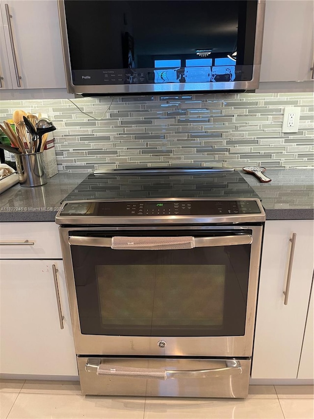 6039 Collins Ave Unit 1525, Miami Beach, FL 33140 - kitchen with appliances with stainless steel finishes, backsplash, dark countertops, and white cabinets