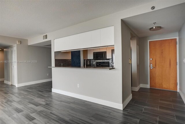 1200 Brickell Bay Dr Unit 2501, Miami, FL 33131 - kitchen featuring black microwave, decorative backsplash, wood tiled floors, white cabinetry, and a textured ceiling