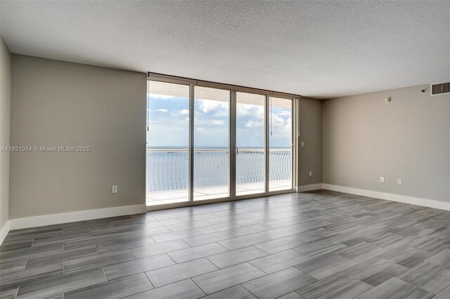 1200 Brickell Bay Dr Unit 2501, Miami, FL 33131 - empty room featuring a textured ceiling, a wall of windows, a water view, and wood finished floors
